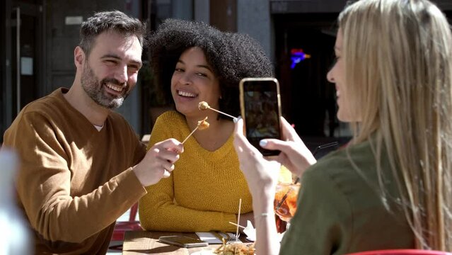 Video of beautiful woman photographing cheerful male and female friends showing food at terrace restaurant