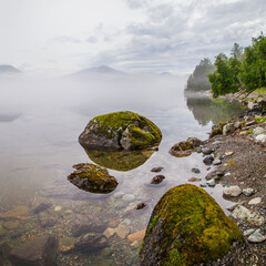 Mountain lake in fog, natural light. Clear water, stones at the bottom. 