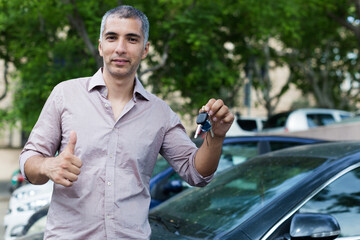 Portrait of male who is standing satisfied with key near his car outdoor.