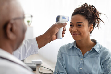 Doctor checking temperature of young black woman using infrared thermometer
