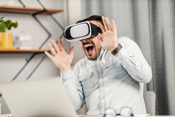 An excited man sitting at home office and having wonderful VR experience.