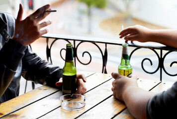 Sharing bad habits.... A cropped image of two young men smoking with beers in front of them.