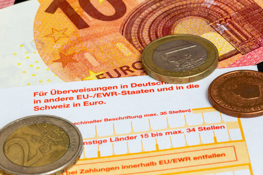 Symbolbild Zahlungsverkehr: Nahaufnahme eines Überweisungsträgers mit Euromünzen und Euroscheinen