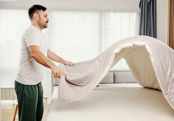 A man making the bed in the morning at his cozy home.