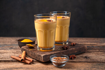 Two glasses of coffee with milk and turmeric on a wooden background