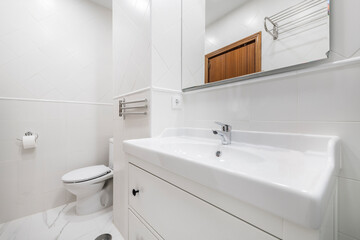 White porcelain sink with white wood cabinet, frameless mirror and white tile
