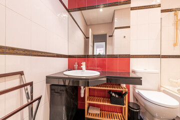 Bathroom with black marble countertop, red details on the tiles and mirror embedded in the wall
