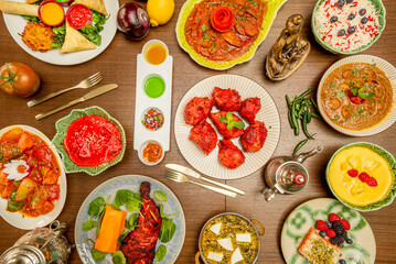 Set of Indian food dishes with chicken tikka masala in the center, meat stuffed samosas, red curry, korma, cinnamon sticks, pilau rice and more spices in jars, carrot cake with red berries and sauces