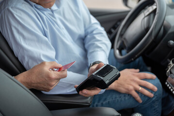unrecognizable cab driver holding a bank payment terminal to process credit card payment purchases - transport concept, cab, taxi and technology - obrazy, fototapety, plakaty