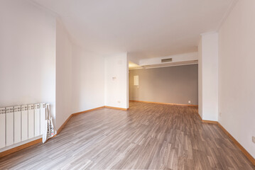 Large empty room with freshly painted walls, ducted air conditioning, white aluminum radiator and oak parquet flooring