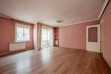 Empty living room with access to a terrace, aluminum radiators, pink painted walls and wooden flooring