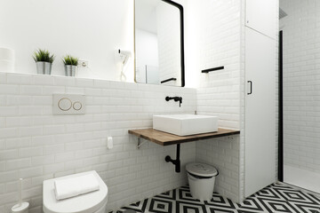 Modern black and white tiled floor cloakroom with white porcelain sink, white tiles, black faucets, black framed mirror on a shelf and blackout shower