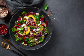 Vitamin salad with beetroot, avocado, feta cheese and pomegranate on a dark background. A healthy, cleansing salad. Top view, copy space.