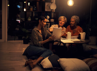 Fototapeta premium This app will help us complete the deadline. Shot of a group of businesswomen working together on a digital tablet in an office at night.
