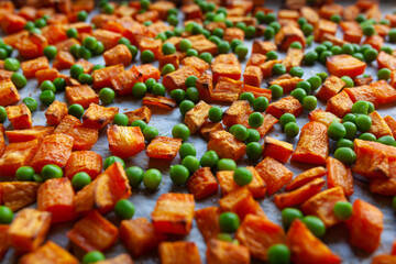Oven roasted carrots and sweet potatoes and green peas on a parchment paper, cut into cubes