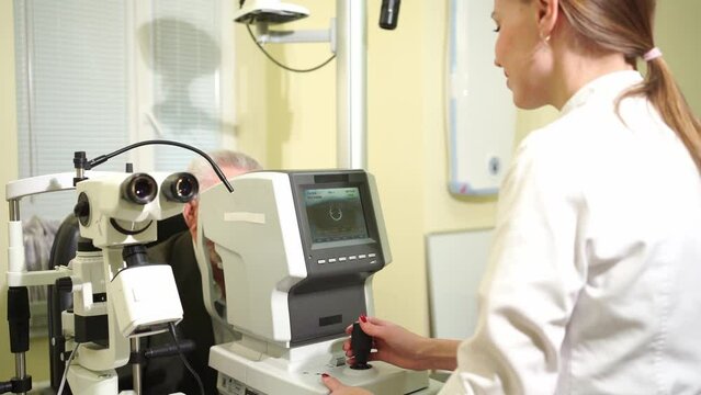 doctor examines elderly man's eye on screen of autorefractometer. 