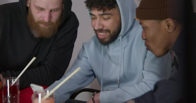 Multiracial friends sit in cozy cafe talking and enjoying drink. African American with Moroccan and white bald bearded man have fun together close view