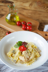 Italian cuisine. Pasta with cheese and white poultry meat. Served in a white plate on a wooden board next to red tomatoes.