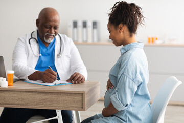 Fototapeta premium Male doctor consulting young smiling pregnant woman