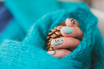 Cow pattern on freshly manicured nails. Creative hand drawn design, bright colors, handmade knitted sweater. Selective focus on the details, blurred background.