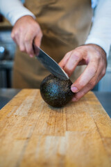 Vertical stock photo of unrecognizable cook slicing an avocado. 