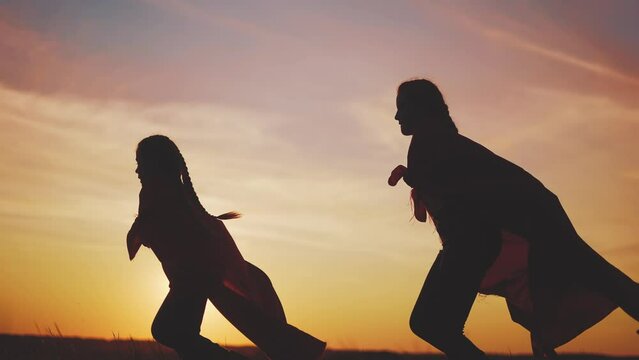 superhero team. kid dream teamwork a business concept. two girls superheroes with cloaks silhouette running in the park silhouette. sunset child superhero playing. team of children working together