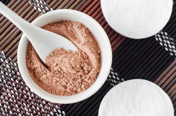 Pink bentonite clay powder in a small white bowl and cotton pads. Clay texture close up. Diy facial or hair mask, dry shampoo recipe. Natural beauty treatment and spa. Top view, copy space