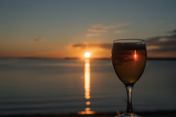 A glass of white wine at sunset, by the sea. Sandy beach, summer, warm evening.