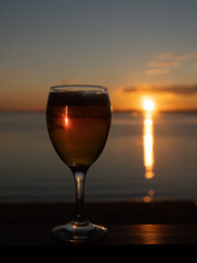 A glass of white wine at sunset, by the sea. Sandy beach, summer, warm evening.