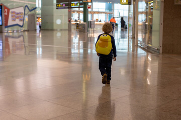 Obraz premium Cute baby boy waiting boarding to flight in airport transit hall near departure gate. Active family lifestyle travel by air with children