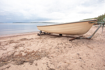 White, plastic boat on the seashore. Sandy beach, summer day.