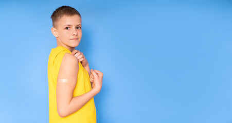 A teenage boy with a patch on his arm clenches his fist and bends his biceps after vaccination....