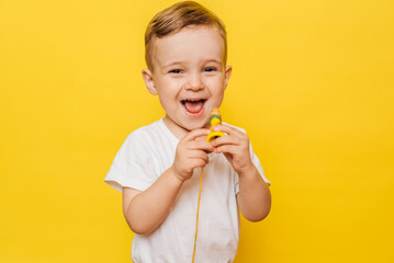 Portrait of a cute laughing little boy on a yellow background with a toy in his hands. Copy space.