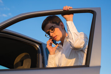 Young beautiful woman calling towing service after her car broke on the road on a sunny day