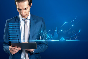 Portrait of attractive european businessman with tablet and abstract business chart hologram on blurry background. Dashboard, investor and finance concept.