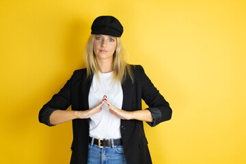 Beautiful woman wearing casual white t-shirt and a cap over isolated yellow background with Hands together and fingers crossed smiling relaxed and cheerful. Success and optimistic
