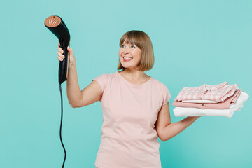 Elderly fun happy housewife woman 50s in pink t-shirt doing housework hold pile of clothes use...