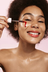 Obraz premium Beauty african woman, naked shoulders and nude face, apply serum vitamin c, argan oil tea tree ingredients in pippette dropper under eye, treating skin for nourishing and moisturizing effect