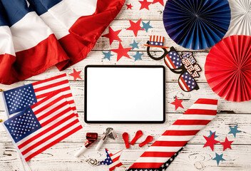 Digital tablet with white screen surrounded with independence day party elements top view flat lay
