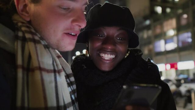 Smiling couple looking at smart phone in city at night, Italy