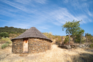 Old cabin or hut with a round shape and slate stone walls and a broom and straw roof