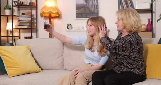 grandmother using cell phone and having fun with her granddaughter taking photos and watching videos