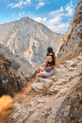 Naklejka na ściany i meble Woman traveler hiking in mountain area sitting on a rock