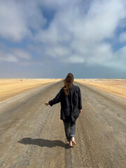 Young woman walks on highway in desert. Girl on center of the road, barefoot.