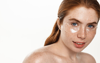 Portrait of plus size woman, redhead girl using under eye patches from dark circles, puffiness, looking happy at camera and smiling, standing over white background