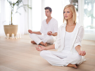 Fototapeta na wymiar Finding inner peace together. Two people sitting in the lotus position in a yoga studio.