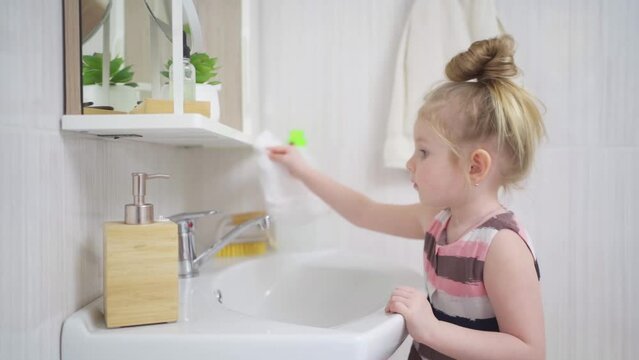 a cute little girl washes sink and the bathroom mirror with a special cleaner.