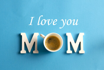 Happy Mother's Day. Mom lettering and cup of coffee on blue background. Flat and top view.