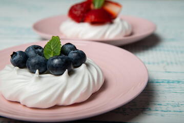 Pavlova cake with strawberries and blueberries and mint on a pink platter. Home confectionery. Old retro white and blue table.
