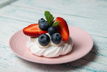 Pavlova cake with strawberries and blueberries and mint on a pink platter. Home confectionery. Old retro white and blue table.